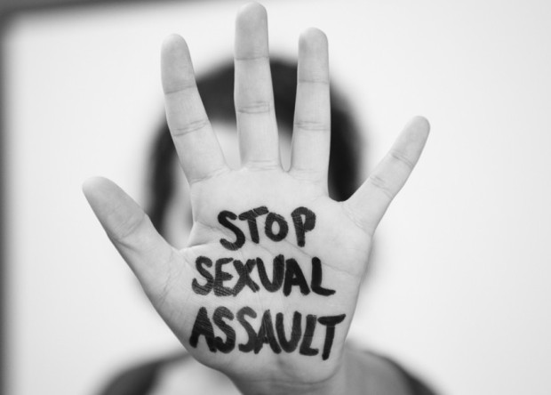 person holding hand up with the words "stop sexual assault" painted on the palm in black and white